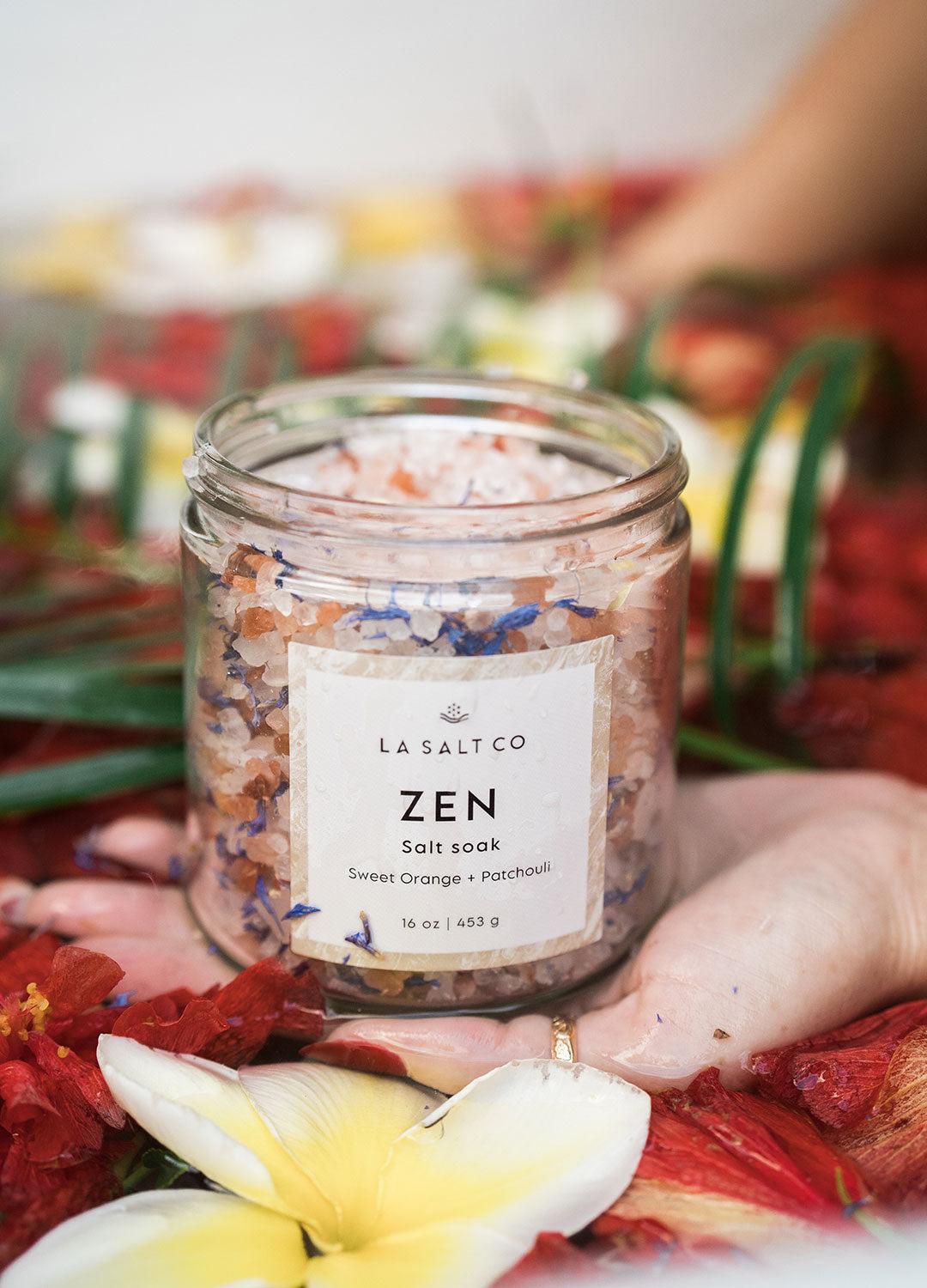 A woman holding a Zen Salt Soak in a floral bath