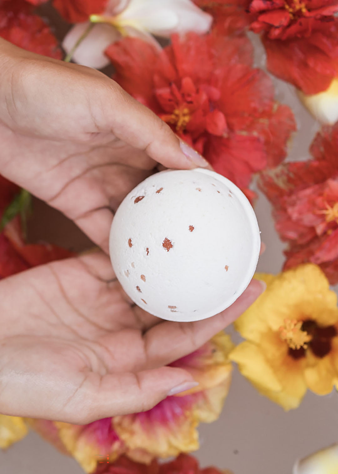 A woman holding a Zen Bath Bomb in a floral bath